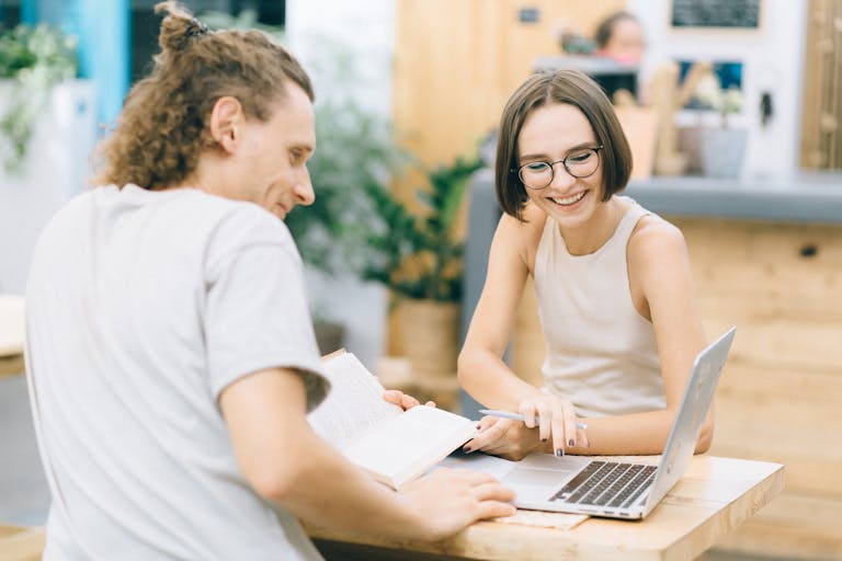 Two young adults smiling and working together indoors, fostering a collaborative environment.